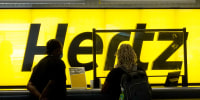 People stand at a Hertz car rental counter